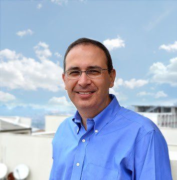 Imagen del director de confa con camisa azul y la ciudad de fondo