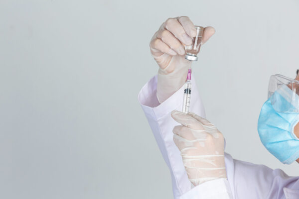 Young doctor is  holding  hypodermic syringe with  vaccine vial  rubber gloves on gray background.