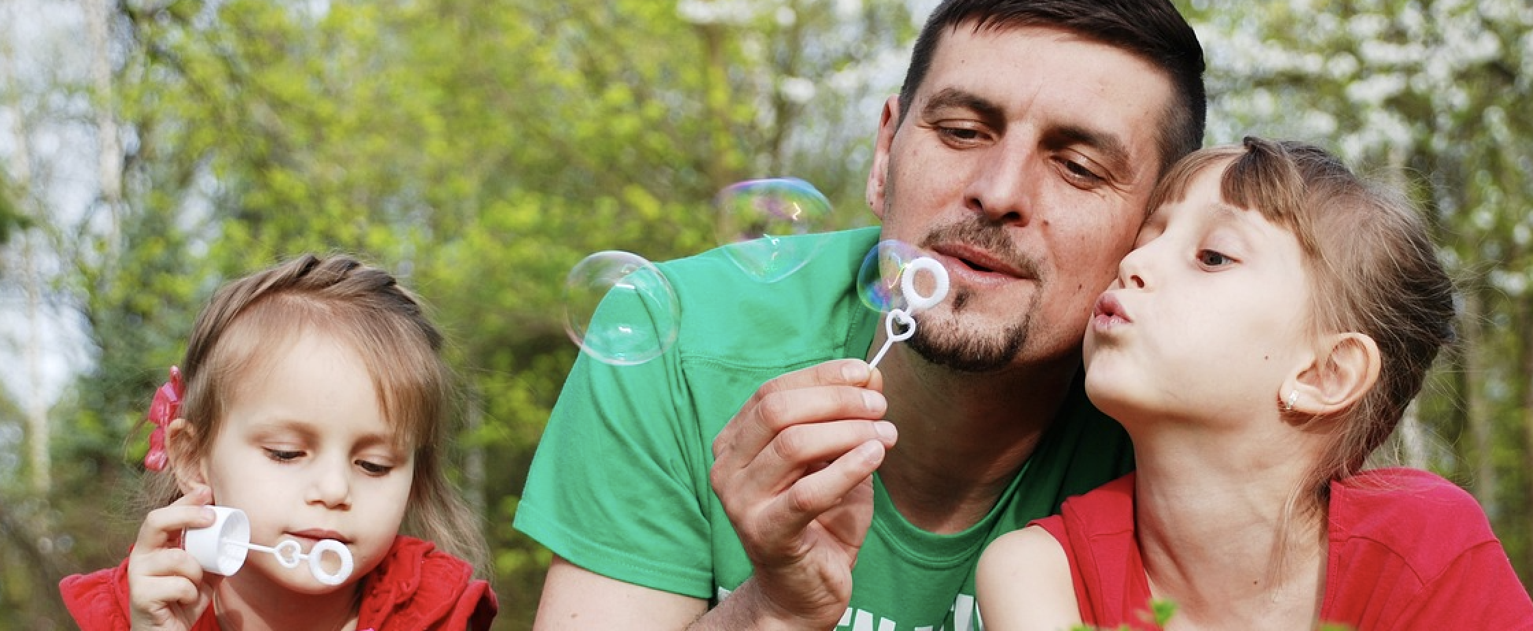 Papá con hijos jugando con burbujas de jabón