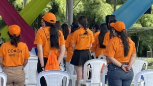 Jóvenes de pie vestidas con camiseta naranja que dice Camper y Coach