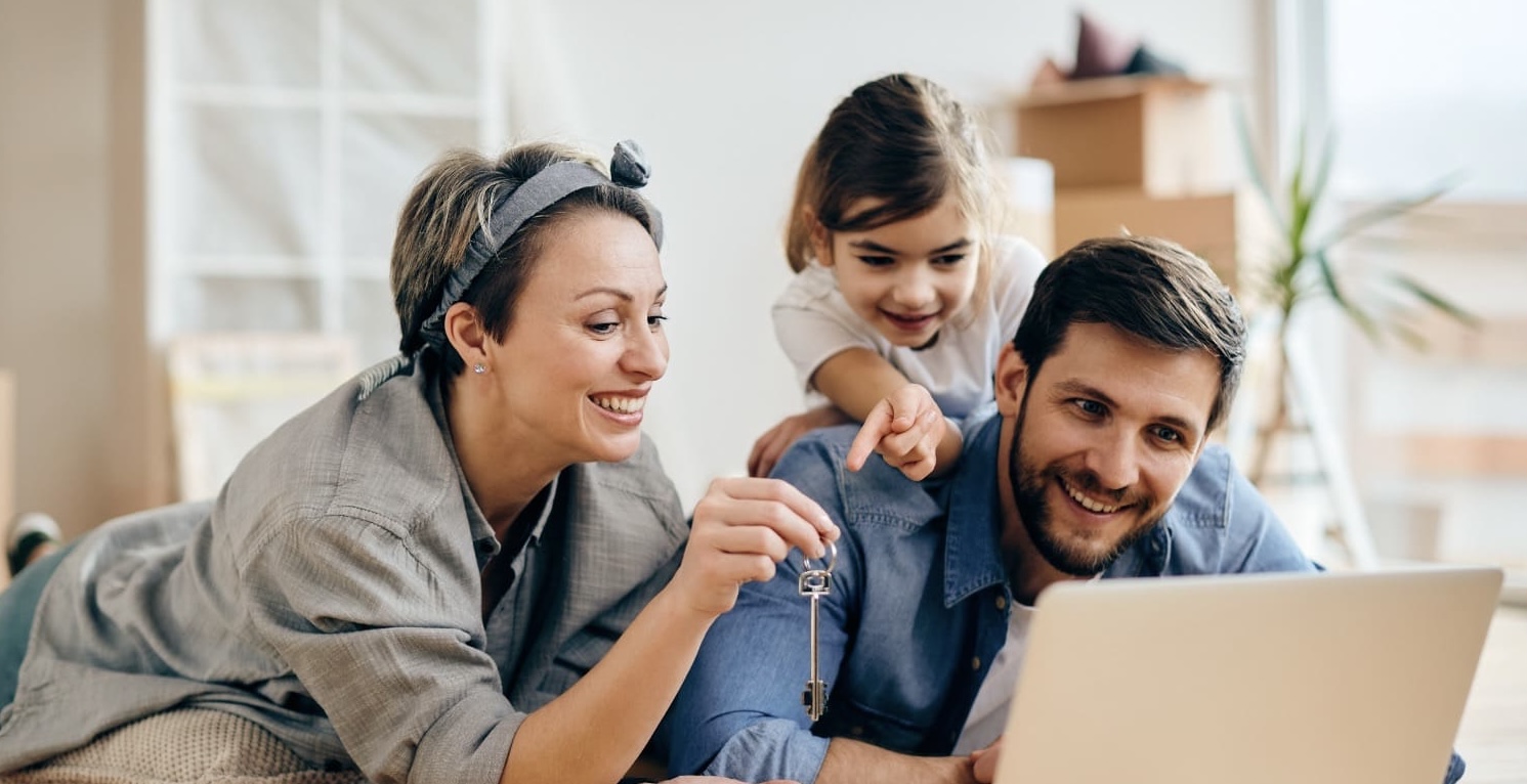 Una familia comparte frente a su computador, sonríen mientras o observan la pantalla