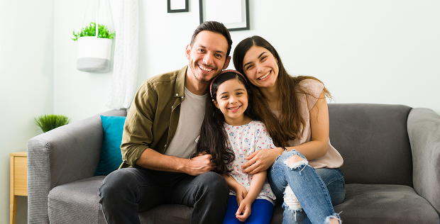 Familia de dos adultos y una niña en un sofá sonriendo a la cámara