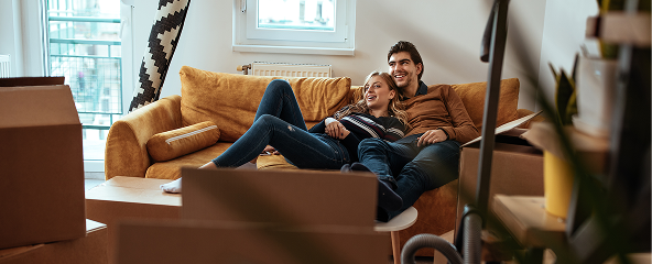 Credito hipotecario Card Una pareja recostados sobre un sofá apreciando sus nuevas compras de su nuevo hogar
