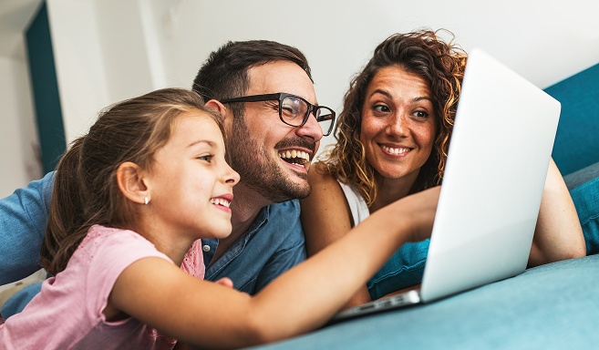 Familia en computador Un hombre con su esposa e hija sonriendo revisando un computador